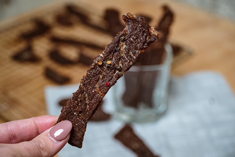 hand holding a piece of peppered beef jerky
