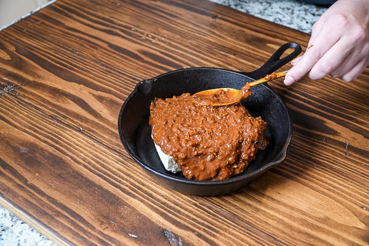 spreading chili over cream cheese in a skillet