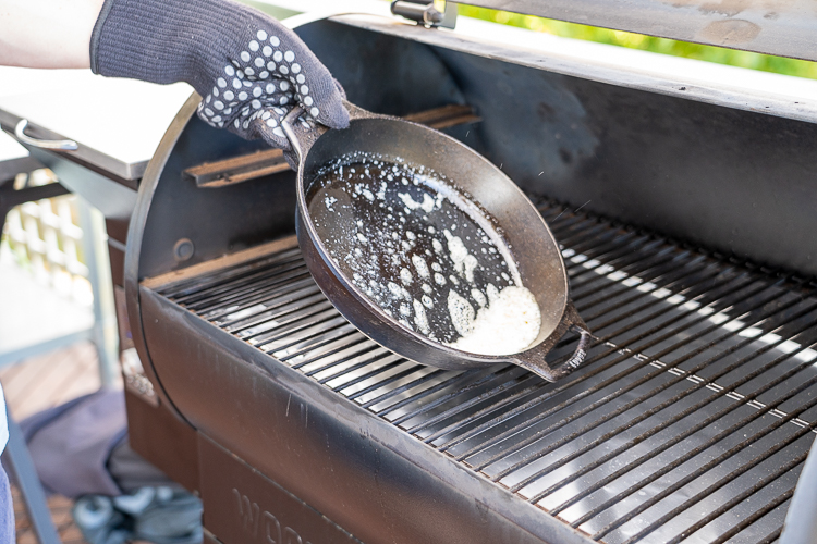a gloved hand holding a hot skillet swirling butter