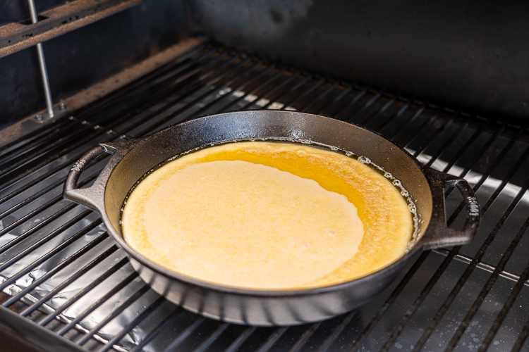 raw cornbread mixture in the skillet on the smoker