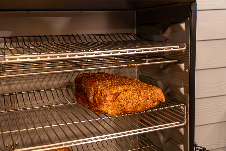 raw seasoned pork butt on a shelf in the smoker