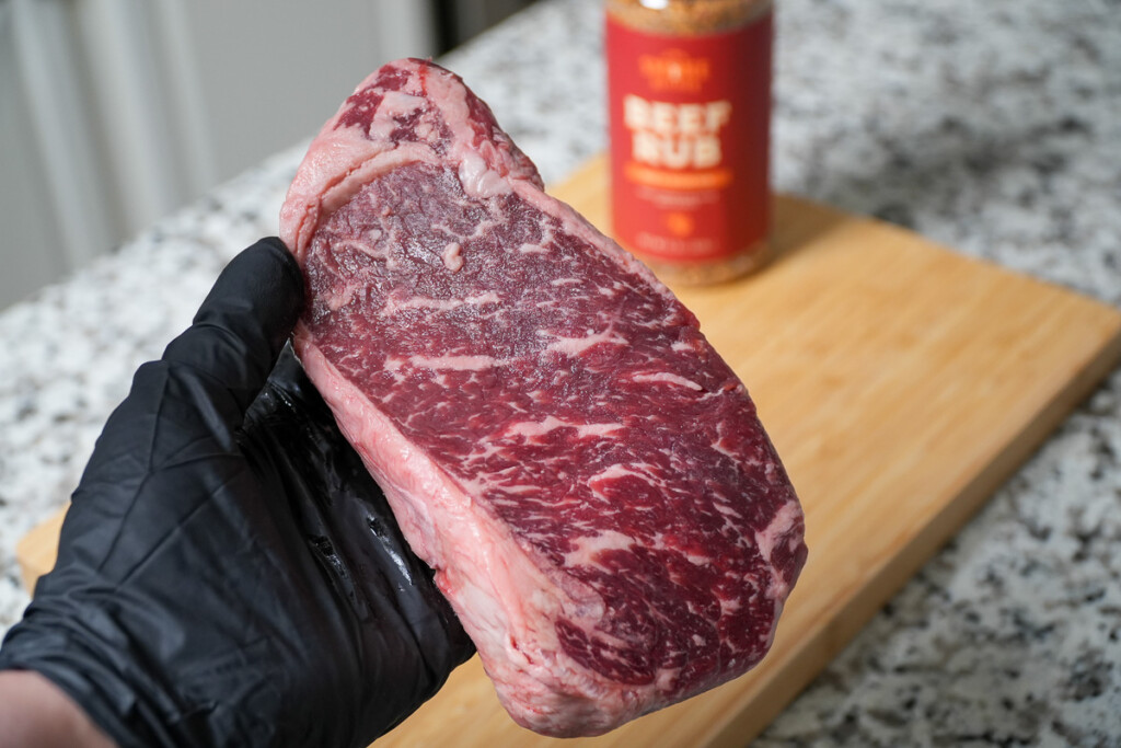 a black glove hand holding a piece of raw steak
