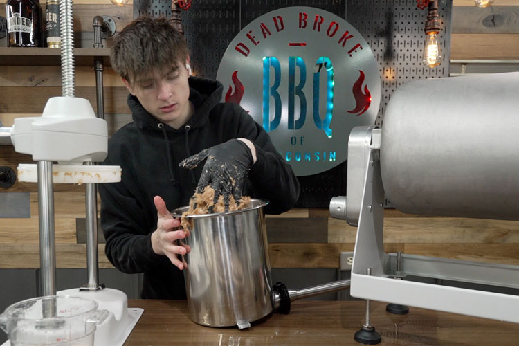 a man filling the sausage stuffer with a black gloved hand