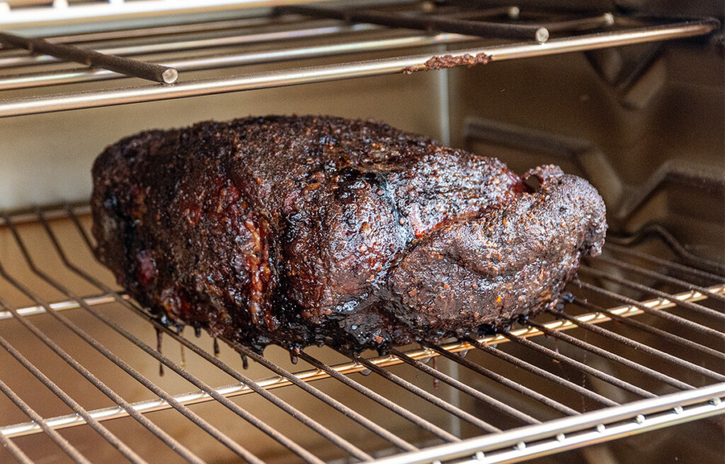 a cooked piece of no wrap pork butt on a shelf in the smoker