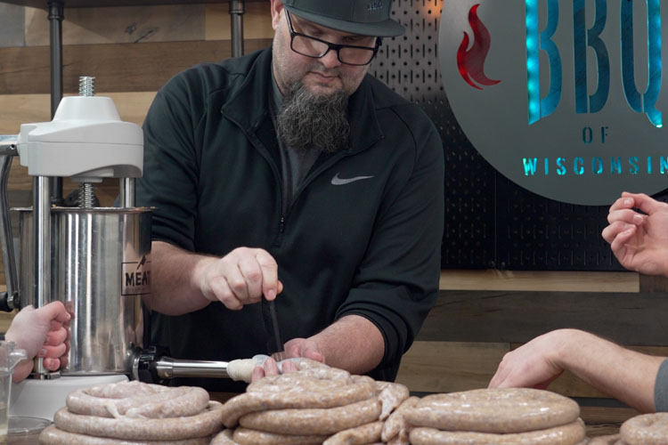 a man pricking sausage as its fed out of the tube to remove air bubbles