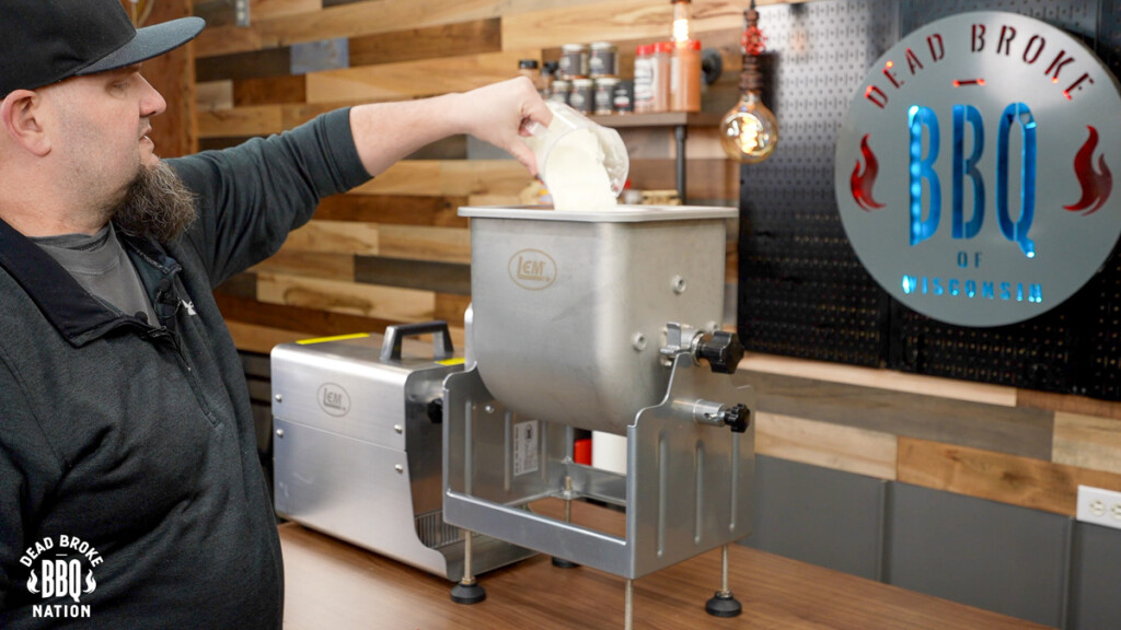 a man pouring milk powder in the barrel of the sausage stuffer