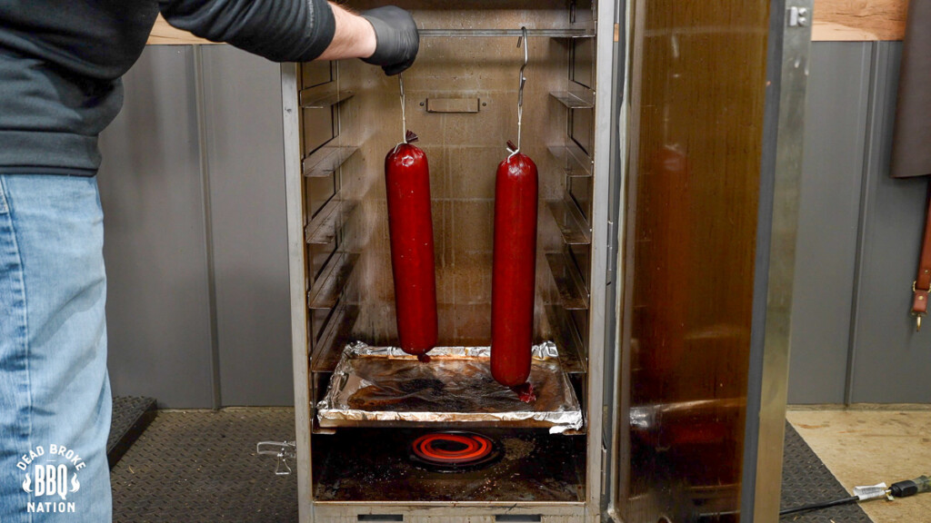 two summer sausages hanging in the smoker