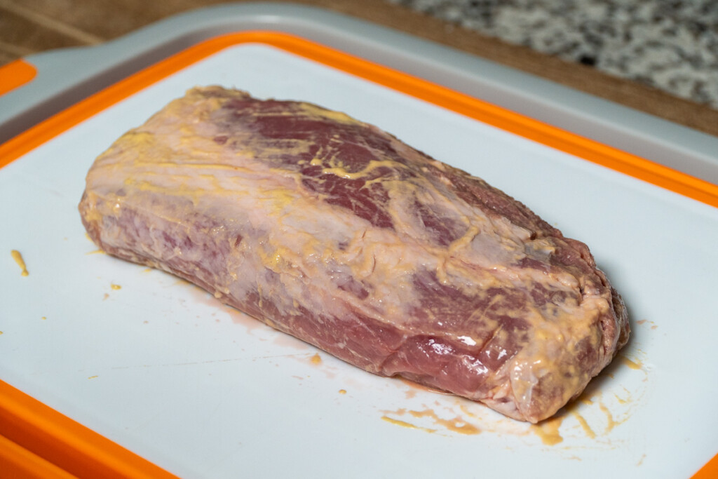 raw pork loin with dijon mustard spread all over it on a white board