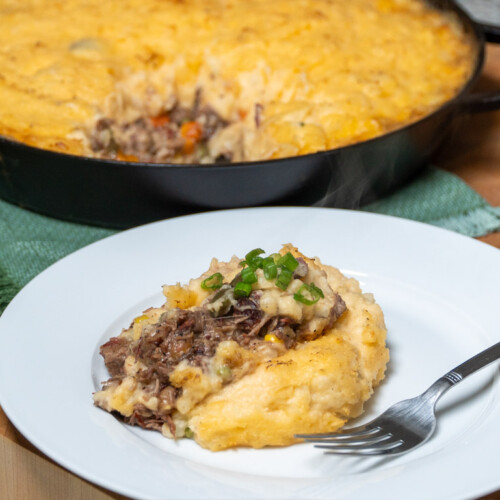 a spoonful of brisket shepherds pie on a white plate with a fork