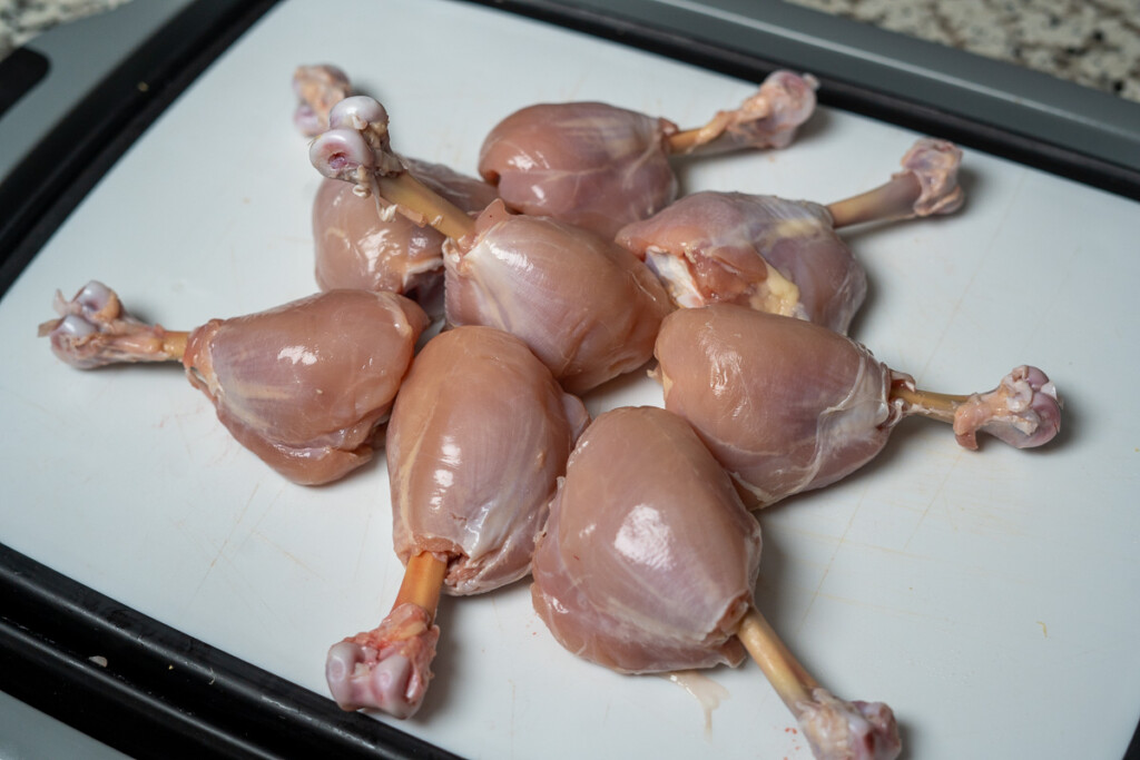 eight skinless, raw chicken lollipops on a white board