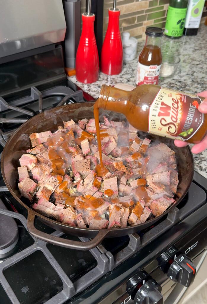 Worstertshire sauce being tipped over brisket in a pan