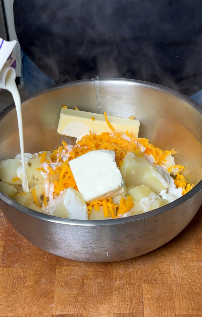 a bowl with potato cubes, cream cheese, cheddar cheese, and milk