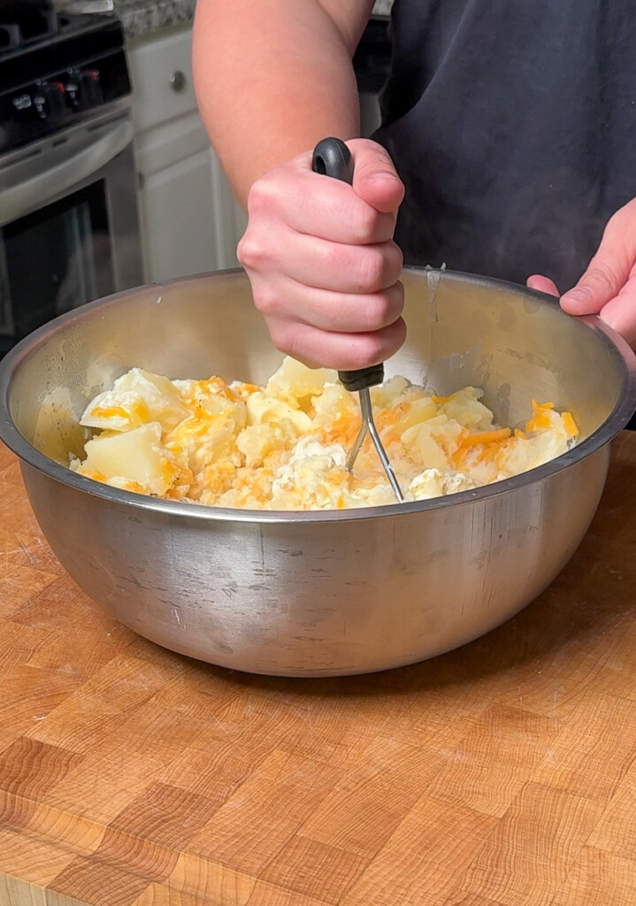 a hand mashing potatoes in a metal bowl
