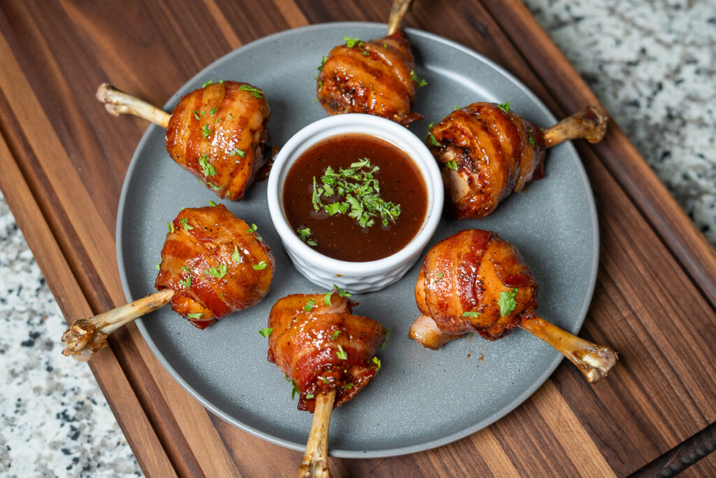 lollipop chicken in a circle on a grey plate with a bowl of dipping sauce in the middle