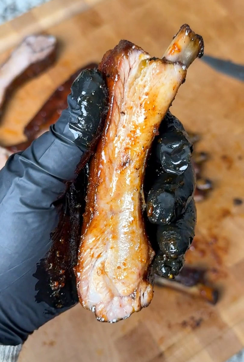 gloved hand holding smoked pork rib