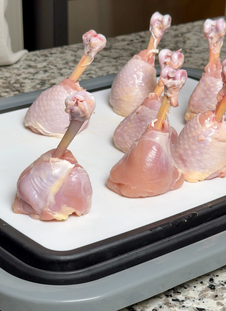 raw chicken lollipops standing upright on a white plate