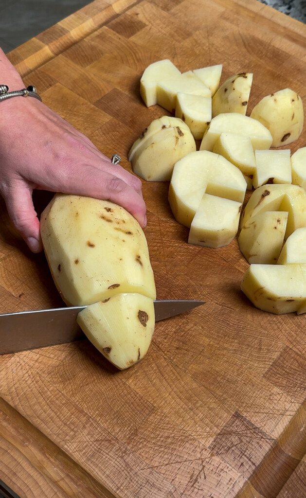 a raw potato being cut into cubes with a knife on a wooden chopping board