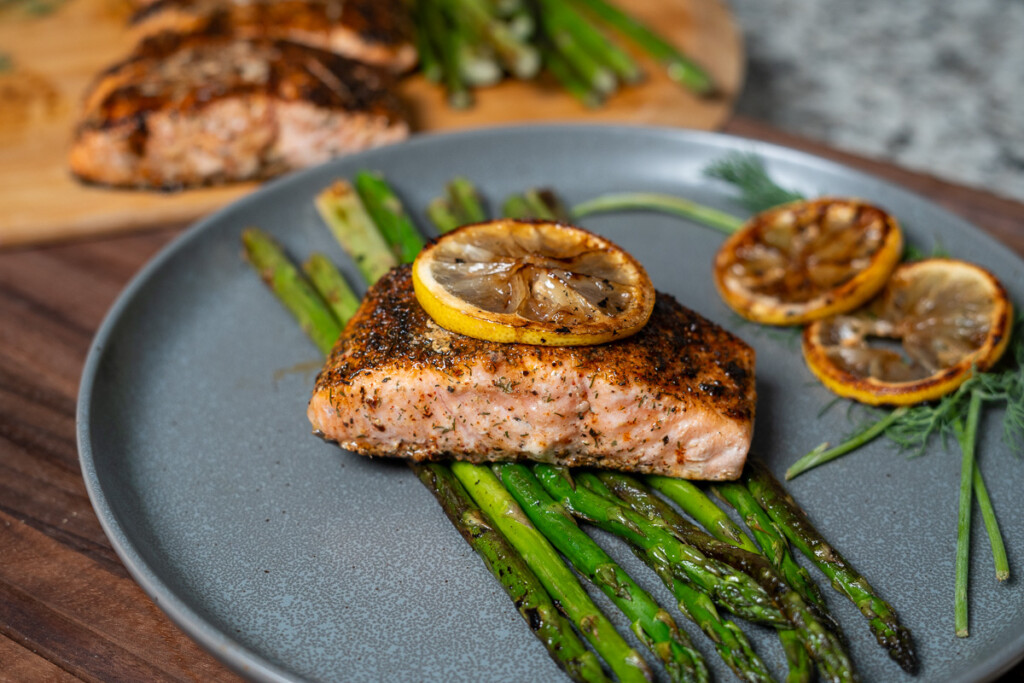 cooked salmon on asparagus with slice of grilled lemon on top