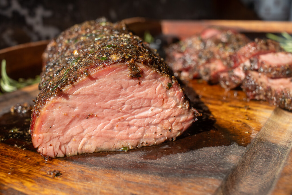 a cross section of a medium rare beef tenderloin with herb crust