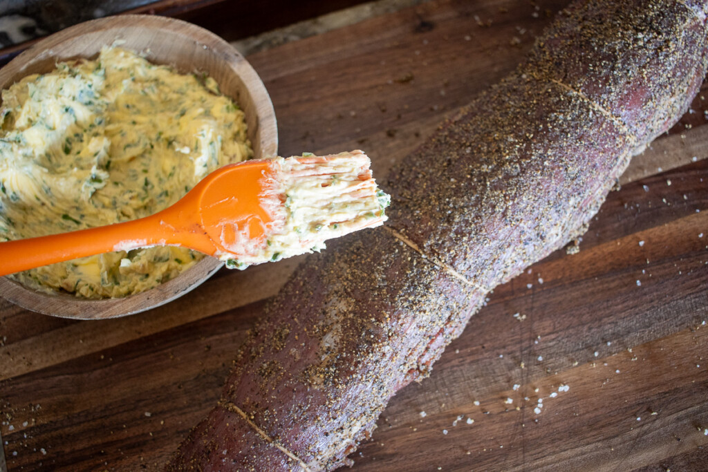 a basting brush cover in butter hovering over a raw beef tenderloin