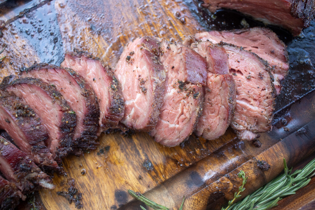 cooked sliced smoked beef tenderloin on a wooden board
