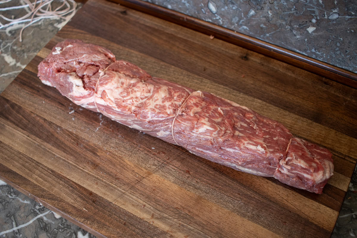 raw beef tenderloin tied in four places with butchers twine, on a wooden board