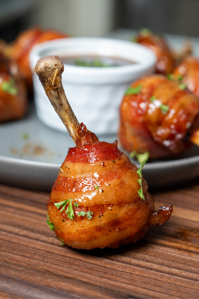 a single smoked chicken lollipop in front of a bowl of dip