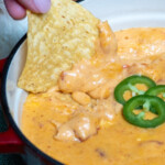 woman holding a tortilla chip dipped in smoked queso dip.