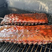 Juicy, glazed pork ribs sizzling on a smoker, perfect for barbecue lovers. Click to explore the best smoked and grilled pork rib recipes.