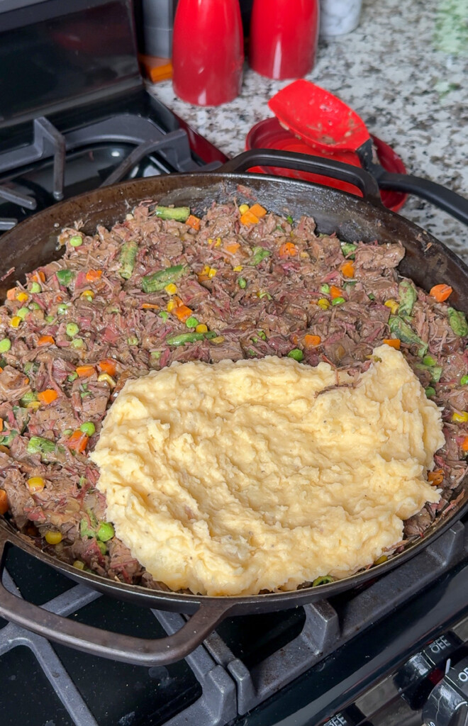 mash potato being spread over meat in a pan