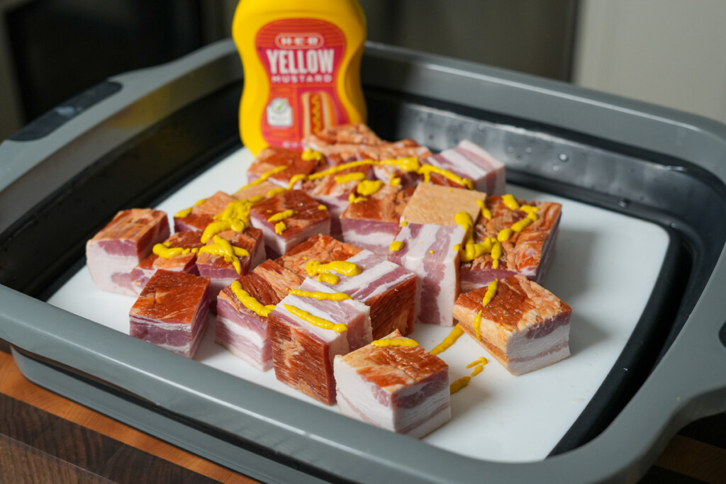 cubes of bacon drizzled with yellow mustard with a bottle of mustard in the background