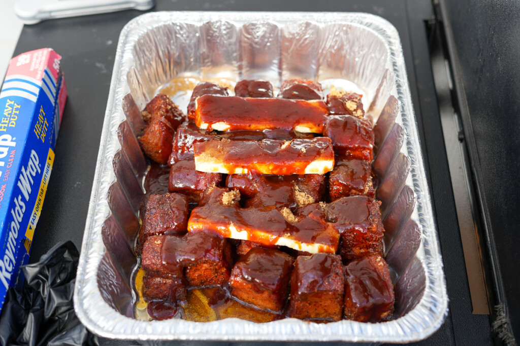 bacon burnt ends in a foil tray with butter, sugar and maple syrup