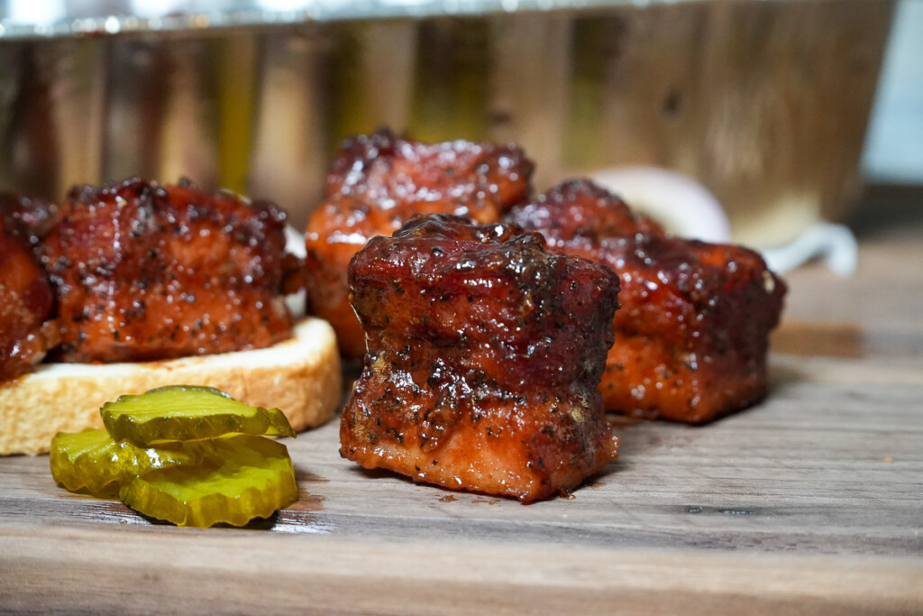 a single cooked burnt bacon end on a wooden board with pickles beside it