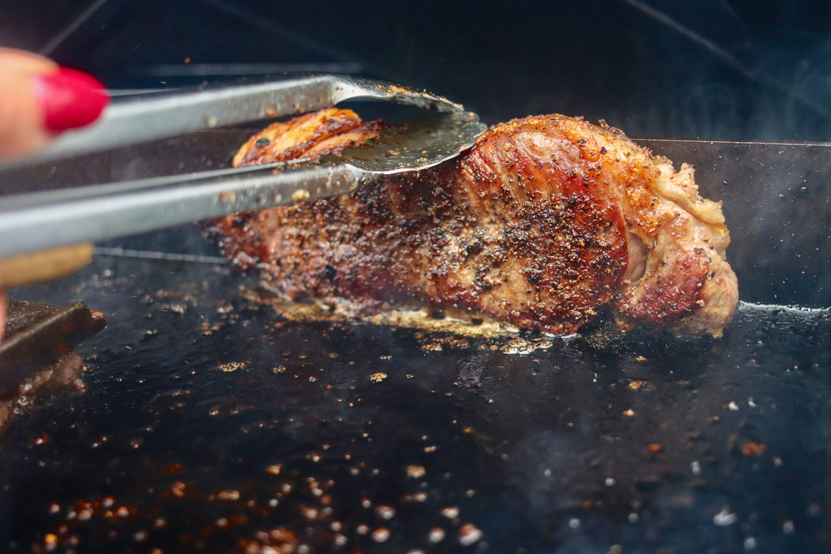 tongs holding a steak on its side searing the fatcap