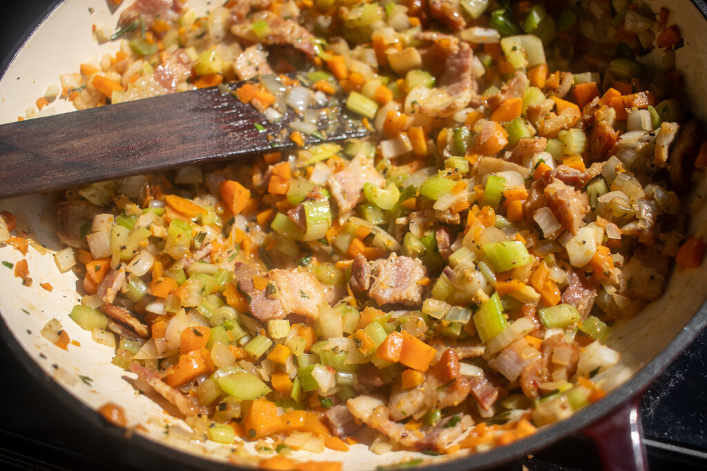 veges and bacon frying in a pan being stirred with wooden spoon