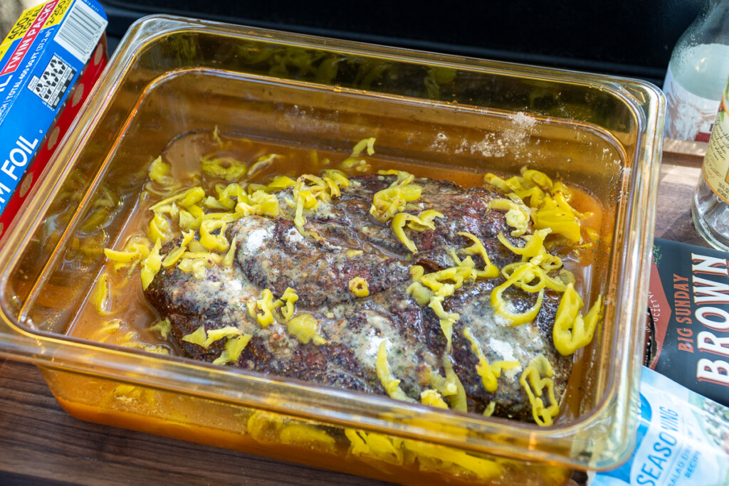 cooked pot roast in a glass dish cover in pepperoncini