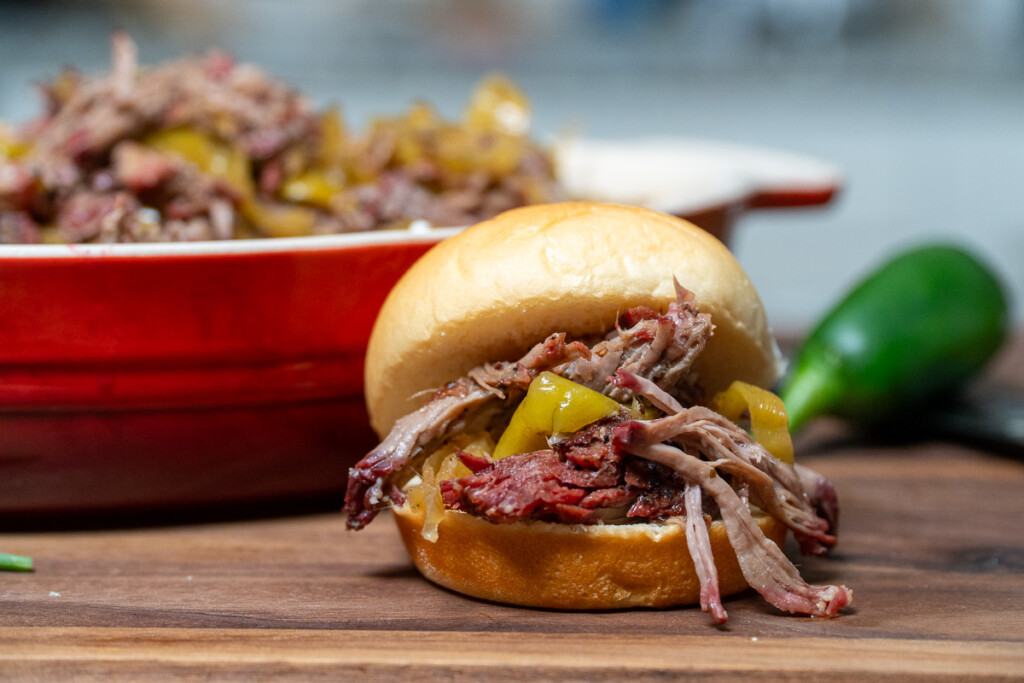 a bun stuffed with meat in front of a red casserole dish