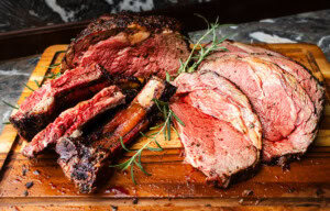 Sliced smoked prime rib with rich bark and medium-rare interior on a wooden cutting board
