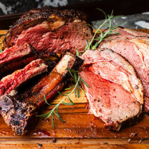Juicy smoked prime rib roast with ribs and slices on cutting board garnished with rosemary