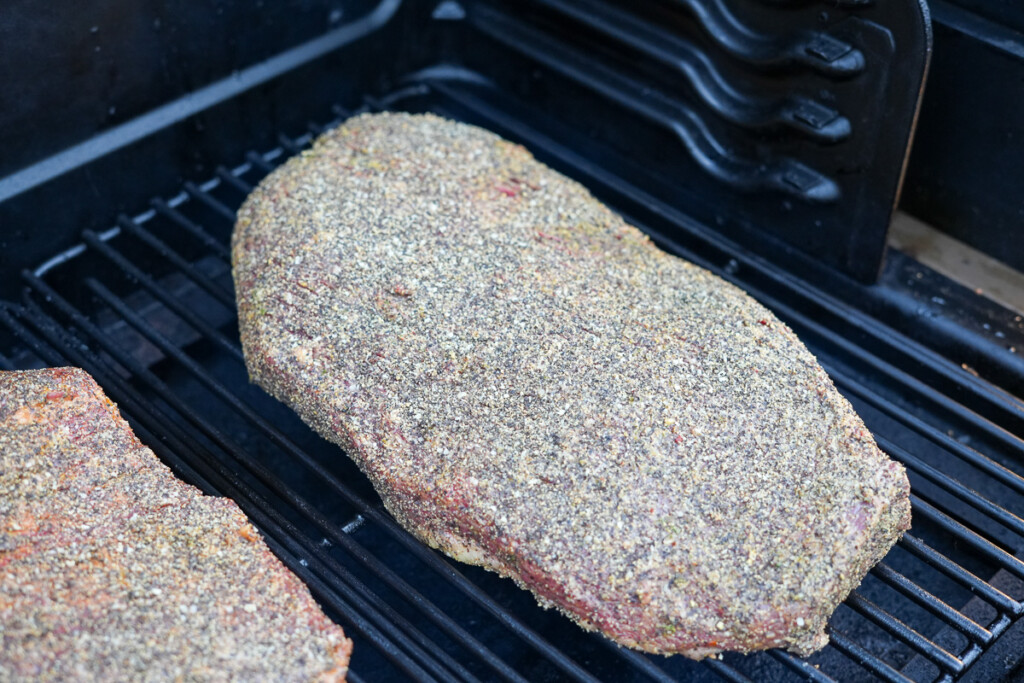 a raw, seasoned piece of brisket flat on the smoker