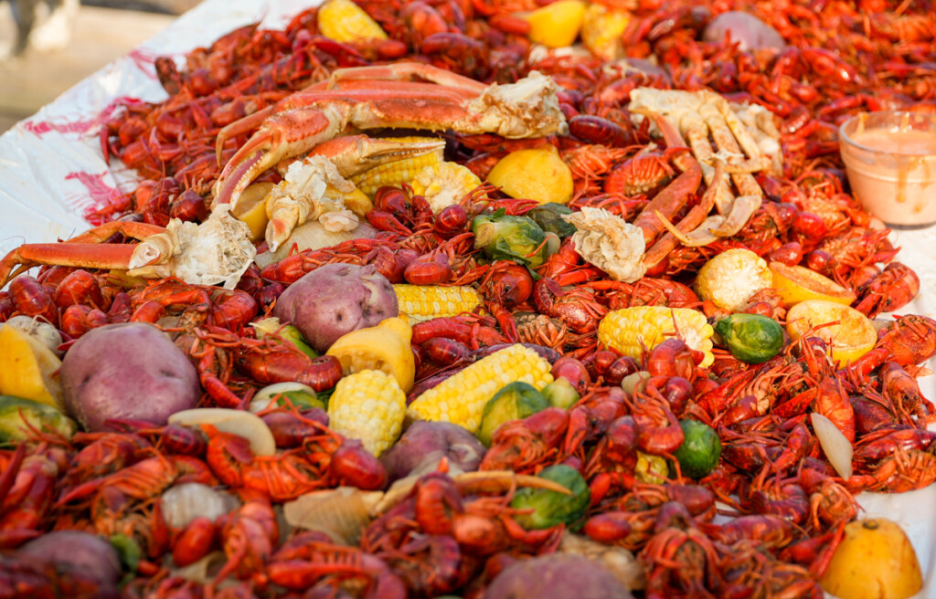 A traditional Louisiana crawfish boil spread across a table, featuring bright red crawfish, corn on the cob, red potatoes, Brussels sprouts, lemons, and crab legs, all seasoned with bold Cajun spices. A bowl of dipping sauce sits on the side, ready for serving.