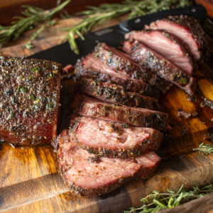 Juicy slices of smoked beef tenderloin with a flavorful herb crust, presented on a wooden cutting board garnished with sprigs of fresh rosemary