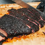 Close-up of sliced smoked beef brisket with a dark, flavorful bark on a wooden cutting board.
