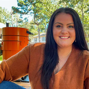 Breanna Stark, barbecue enthusiast, social media personality (@Marriedtobbq), and author at Smoked BBQ Source, smiling outdoors in a brown sweater sitting in front of a smoker.