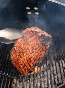 tongs holding steak over a hot charcoal grill