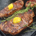 Perfectly grilled steaks sizzling on the grill, topped with melting butter and fresh herbs.