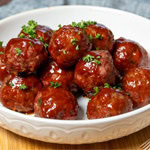 Glazed smoked beef meatballs served in a white bowl, garnished with fresh parsley.