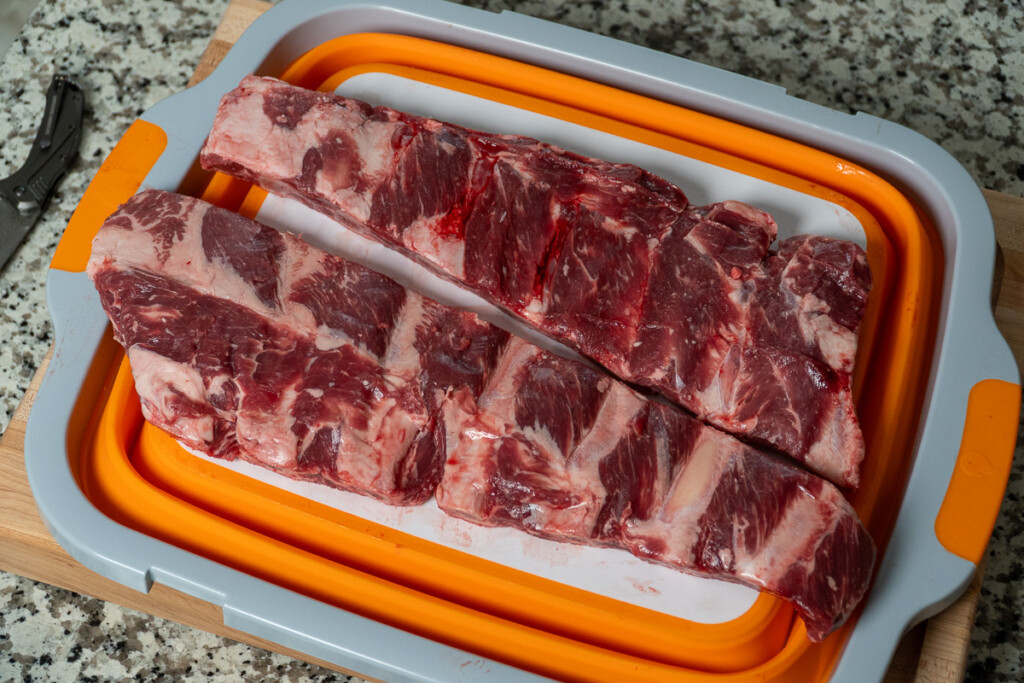 two slabs of raw beef back ribs on a white and orange board