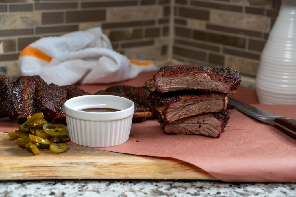 a bowl of sauce and three smoked beef back ribs stacked on top of each other