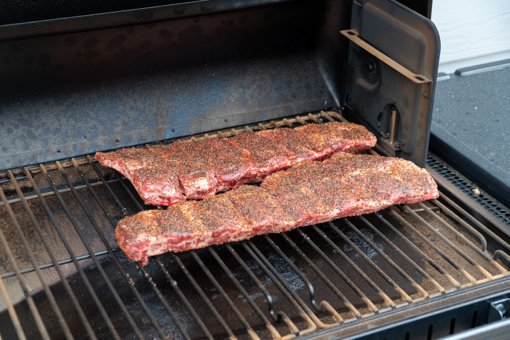 two slabs of raw seasoned beef back ribs on the smoker grill